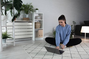 Nilüfer pozisyonunda oturan mutlu ve çekici genç bir kadın antrenörle internetten yoga kursuna başlıyor ya da uzaktan antrenör olarak Webinar seansı yapıyor..