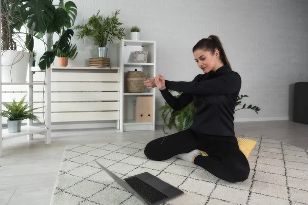 Nilüfer pozisyonunda oturan mutlu ve çekici genç bir kadın antrenörle internetten yoga kursuna başlıyor ya da uzaktan antrenör olarak Webinar seansı yapıyor..