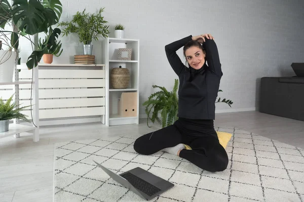 Nilüfer pozisyonunda oturan mutlu ve çekici genç bir kadın antrenörle internetten yoga kursuna başlıyor ya da uzaktan antrenör olarak Webinar seansı yapıyor..