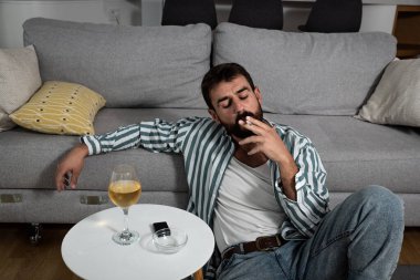 Alkolik bir adam elinde alkollü bir sigarayla masanın üstünde sigara içiyor. Bağımlılık konsepti. Erkek bağımlı evde tek başına alkol ve sigara içiyor