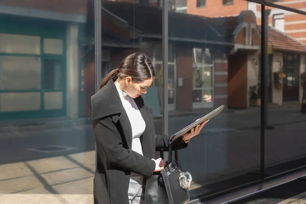 Young business woman on formal wear standing outdoor in front of the building searching her office keys or car keys in her purse that she lost. Person search for her smartphone in her handbag.