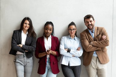 Ofiste kollarını kavuşturmuş duran iş adamlarının portresi. Bir grup iş arkadaşı ofis binasında kendine güvenen bir yüz ifadesiyle gülümsüyor..
