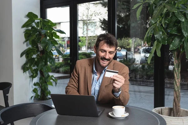 Young business man in casual clothing ordering online with his credit card on his laptop computer. Freelancer is happy because bank give him bigger limit for money to spend.