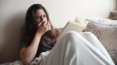 Genç hasta kadın kitap öksürüğü okuyarak ve nezleden hapşırarak yatakta yatıyor. Genç hasta dişilerin soğuk algınlığı ve yüksek sıcaklıkta grip sorunları var..