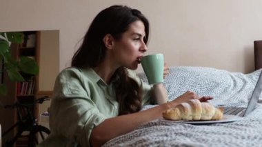 İlk kahvesini içen serbest çalışan genç iş kadını kahvaltıda kruvasan yiyor ve dizüstü bilgisayarı üzerinde çalışıyor. Yurtdışından gelen bir kadın bilgisayarını kullanarak sabah haberlerini kontrol ediyor..