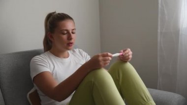 Genç sinirli kadın elinde hamilelik testi ile evde oturuyor ve sabırsızlıkla test sonuçlarını bekliyor. Belki hamile belki de değil.