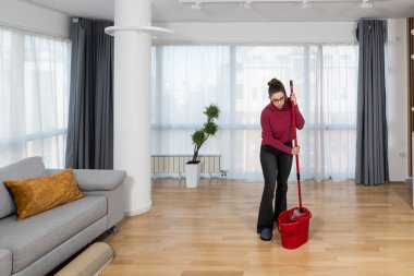 Young landlady is making a big cleaning for the apartment she is renting out, to be clean for the new tenants to whom she has rented out the apartment. Teenage girl or woman rubbing the floor.