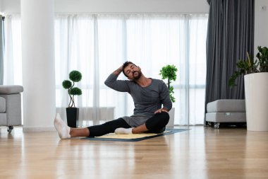 Happy attractive young business man in active sport wear sitting on floor stretching muscles at his apartment after or before the work, training yoga class. Home workout as stress and pain relief.