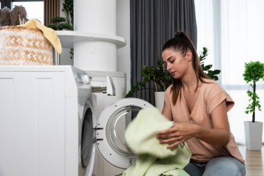 Young woman or housewife putting clothes and laundry to the washing machine to wash the stuff to be clean and fresh. Girl work as a maid to pay her college bills washing laundry.
