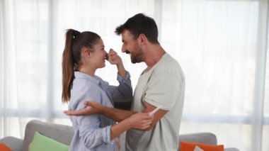 Young happy couple hugging and kissing after they realize that they will have a baby. Pregnant woman hugging her man holding positive pregnancy test stick in her hand.
