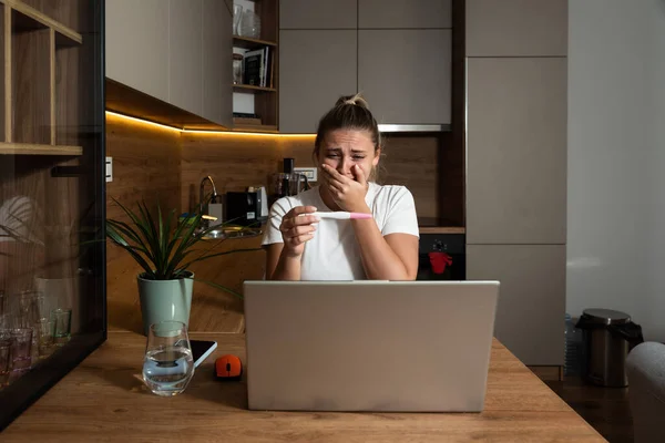 Young woman surprised negative facial reactions on positive result on pregnancy test. Young girl talking on video call on laptop computer with her mother complaining that she is pregnant. Unwanted