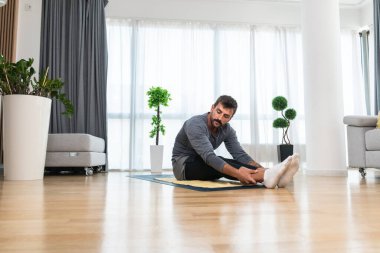 Young man rehabilitation exercise at home after car crash accident. Recovery workout of young guy with yoga training poses for stretching the muscles. Physical therapy exercising