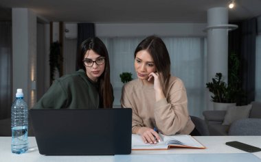 Two young college students study together helping each other with lection for exam. Roommates doing homework together in their apartment, reading and searching the internet for answers. Education 