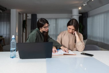 Two young college students study together helping each other with lection for exam. Roommates doing homework together in their apartment, reading and searching the internet for answers. Education 