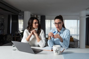 Two young college students study together helping each other with lection for exam. Roommates doing homework together in their apartment, reading and searching the internet for answers. Education 