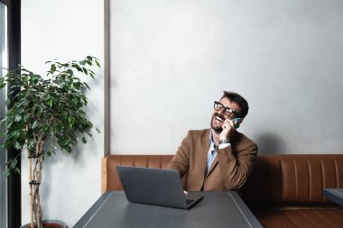 Kafeteryada oturan başarılı genç iş adamı kahve içiyor ve borsa fiyatlarının yükselmesinden mutlu görünüyor. Erkek, çevrimiçi ticaret ve finans sektöründe başarıyla zengin oluyor..