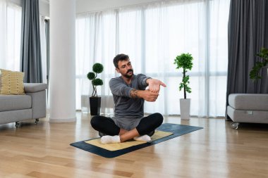Kanserden kurtulan genç adam evde yoga antrenmanı yapıyor, kaslarını esnetiyor ve uzun süre acı ve hastalıkla mücadele ettikten sonra sağlıklı bir yaşam için egzersiz yapıyor..