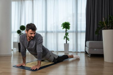 Kanserden kurtulan genç adam evde yoga antrenmanı yapıyor, kaslarını esnetiyor ve uzun süre acı ve hastalıkla mücadele ettikten sonra sağlıklı bir yaşam için egzersiz yapıyor..