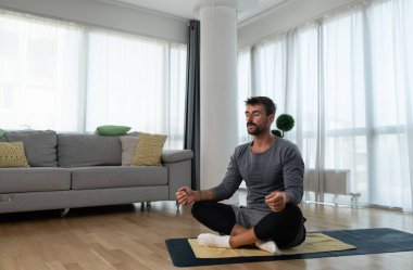 Kanserden kurtulan genç adam evde yoga antrenmanı yapıyor, kaslarını esnetiyor ve uzun süre acı ve hastalıkla mücadele ettikten sonra sağlıklı bir yaşam için egzersiz yapıyor..