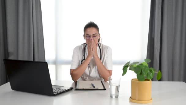 ストレスの多い仕事から休憩しながら病院の事務室に座っている若いうつ病女性医師 精神的な圧力の下で働く女性医療従事者は診療所での勤勉な仕事から一人で休んでいます — ストック動画