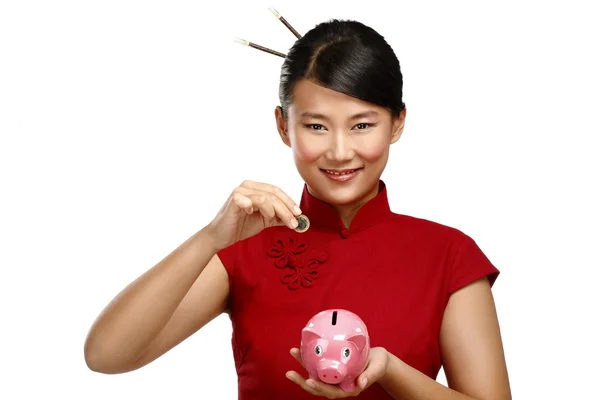 Traditionel asiatisk kvinde gemmer en mønt i en grisebank - Stock-foto