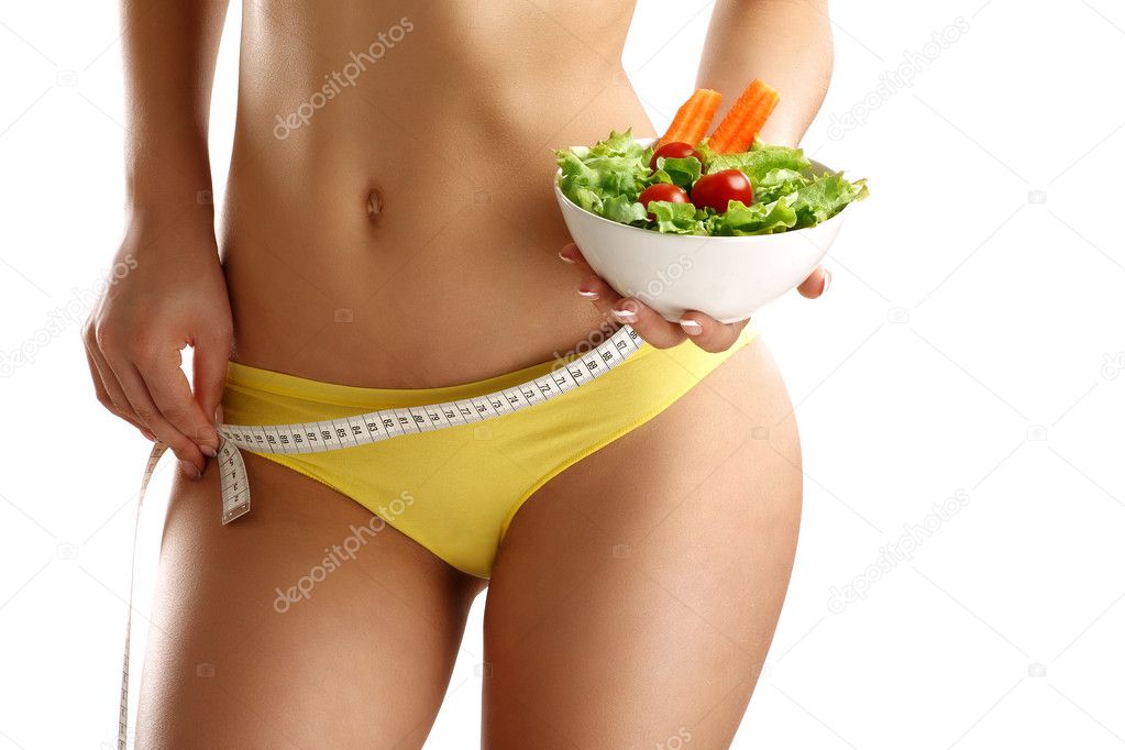 Close up of a woman measuring  hips with a salad in her hand