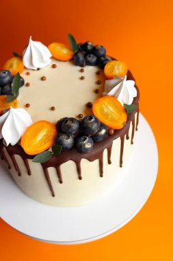Parlak doğum günü pastası. Çikolata lekeleri ve meyveler. Tahta beyaz bir standın üzerinde turuncu arka planda.
