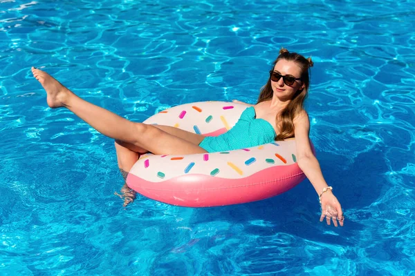 Bikinili genç bir kadın havuzda şişme suda yüzüyor.