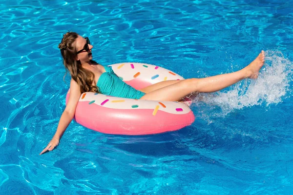 Bikinili genç bir kadın havuzda şişme suda yüzüyor.