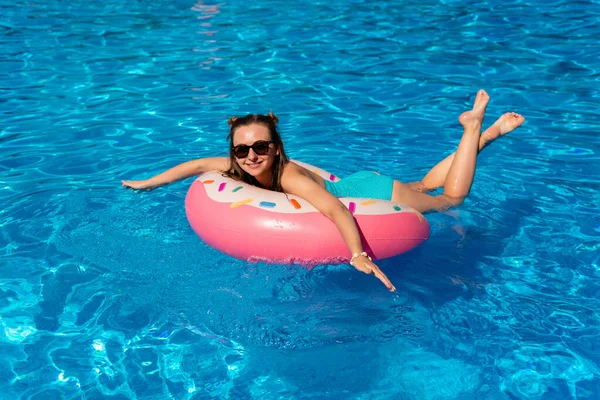 Bikinili genç bir kadın havuzda şişme suda yüzüyor.