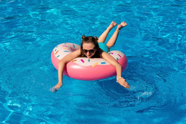 Bikinili genç bir kadın havuzda şişme suda yüzüyor.