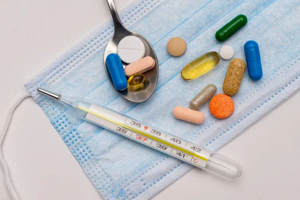 colored pills and vitamins with an electronic  thermometer on a white background