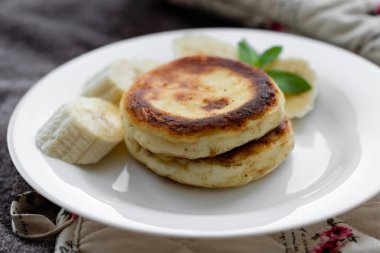 Two cottage cheese pancakes with sliced banana in a white plate. Traditional breakfast or lunch. Traditional Ukrainian breakfast.