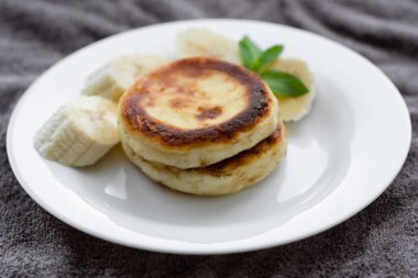 Two cottage cheese pancakes with sliced banana in a white plate. Traditional breakfast or lunch. Traditional Ukrainian breakfast.