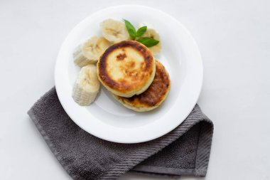 Two cottage cheese pancakes with sliced banana in a white plate. Traditional breakfast or lunch. Traditional Ukrainian breakfast.