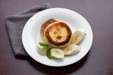 Two cottage cheese pancakes with sliced banana in a white plate. Traditional breakfast or lunch. Traditional Ukrainian breakfast.