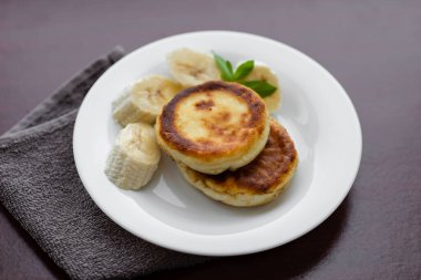 Two cottage cheese pancakes with sliced banana in a white plate. Traditional breakfast or lunch. Traditional Ukrainian breakfast.