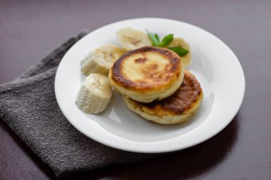 Two cottage cheese pancakes with sliced banana in a white plate. Traditional breakfast or lunch. Traditional Ukrainian breakfast.