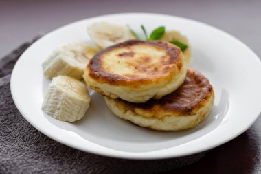 Two cottage cheese pancakes with sliced banana in a white plate. Traditional breakfast or lunch. Traditional Ukrainian breakfast.