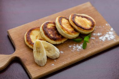 Several cottage cheese pancakes with sliced bananas on a wooden plank. Traditional breakfast or lunch. Traditional Ukrainian breakfast.