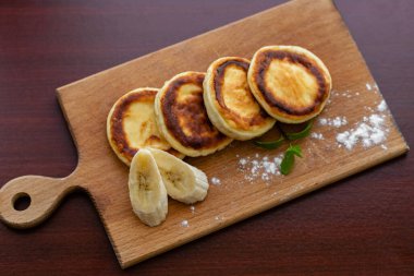 Several cottage cheese pancakes with sliced bananas on a wooden plank. Traditional breakfast or lunch. Traditional Ukrainian breakfast.