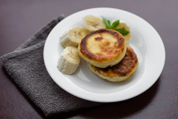 Two cottage cheese pancakes with sliced banana in a white plate. Traditional breakfast or lunch. Traditional Ukrainian breakfast.