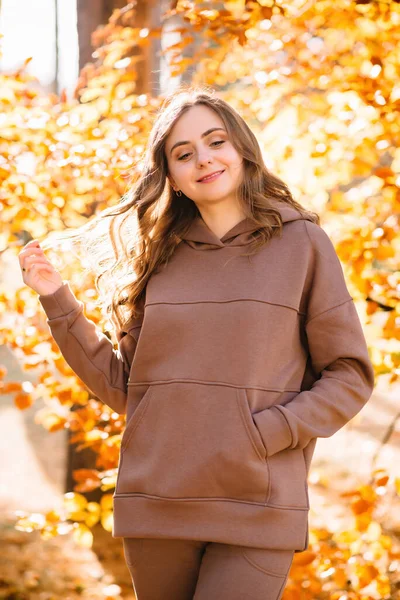 Young woman in hoodie smiling in an autumn park. Sunny weather. Fall season.