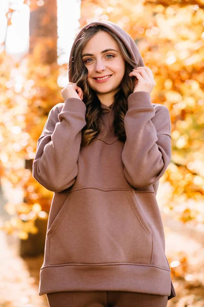 Young woman in hoodie in autumn park. Sunny weather. Fall season.