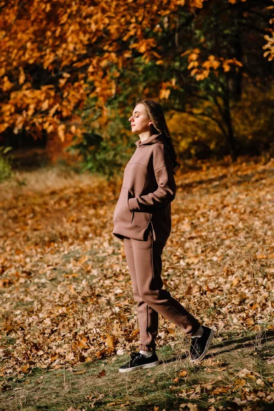 Young woman in hoodie smiling and enjoying warm autumn days in an autumn park. Sunny weather. Fall season.