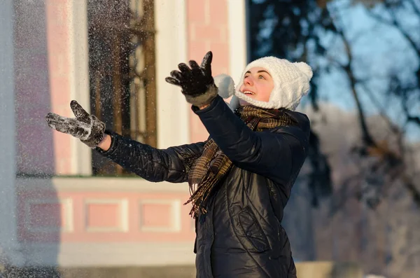暖かいニットの帽子をかぶって雪の冬の公園で笑顔と雪を吹いて幸せな若い女性 天気は晴れ 冬の季節 ストック画像