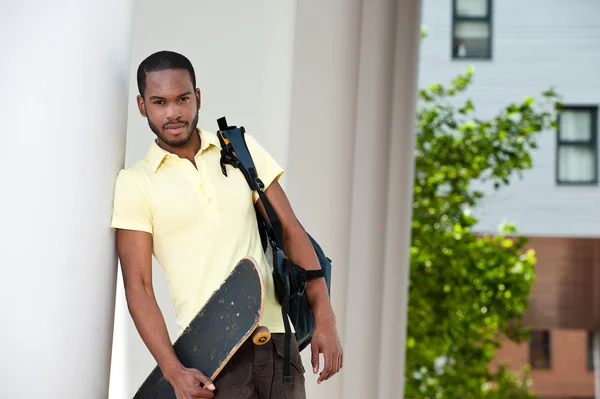 Портрет молодого черного мужчины со скейтбордом и сумкой — стоковое фото