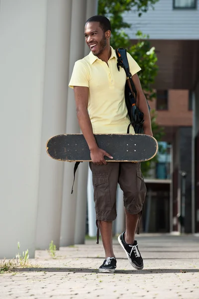 Черный мужчина со скейтбордом и сумкой — стоковое фото