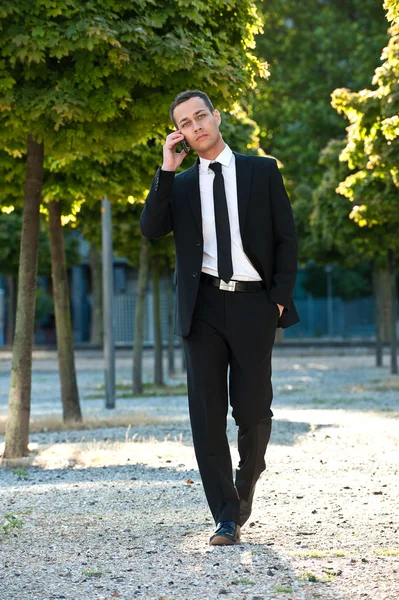 Uomo d'affari che cammina nel parco con il cellulare — Foto Stock