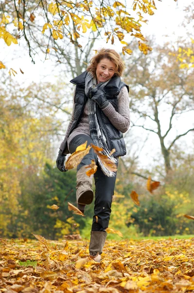 Mujer pateando hojas amarillas en otoño — Foto de Stock